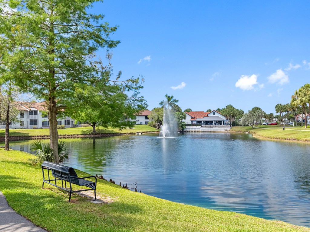A serene park with a bench, a fountain, and a clear blue sky.